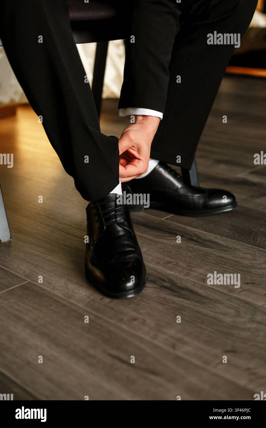 Mann in schwarzen Anzughosen, der seinen schwarzen Lederschuh auf Holzboden anpasst. Eleganter Bräutigam macht sich bereit, formelle männliche Bekleidung, luxuriöses Geschäftsschuhwerk Stockfoto