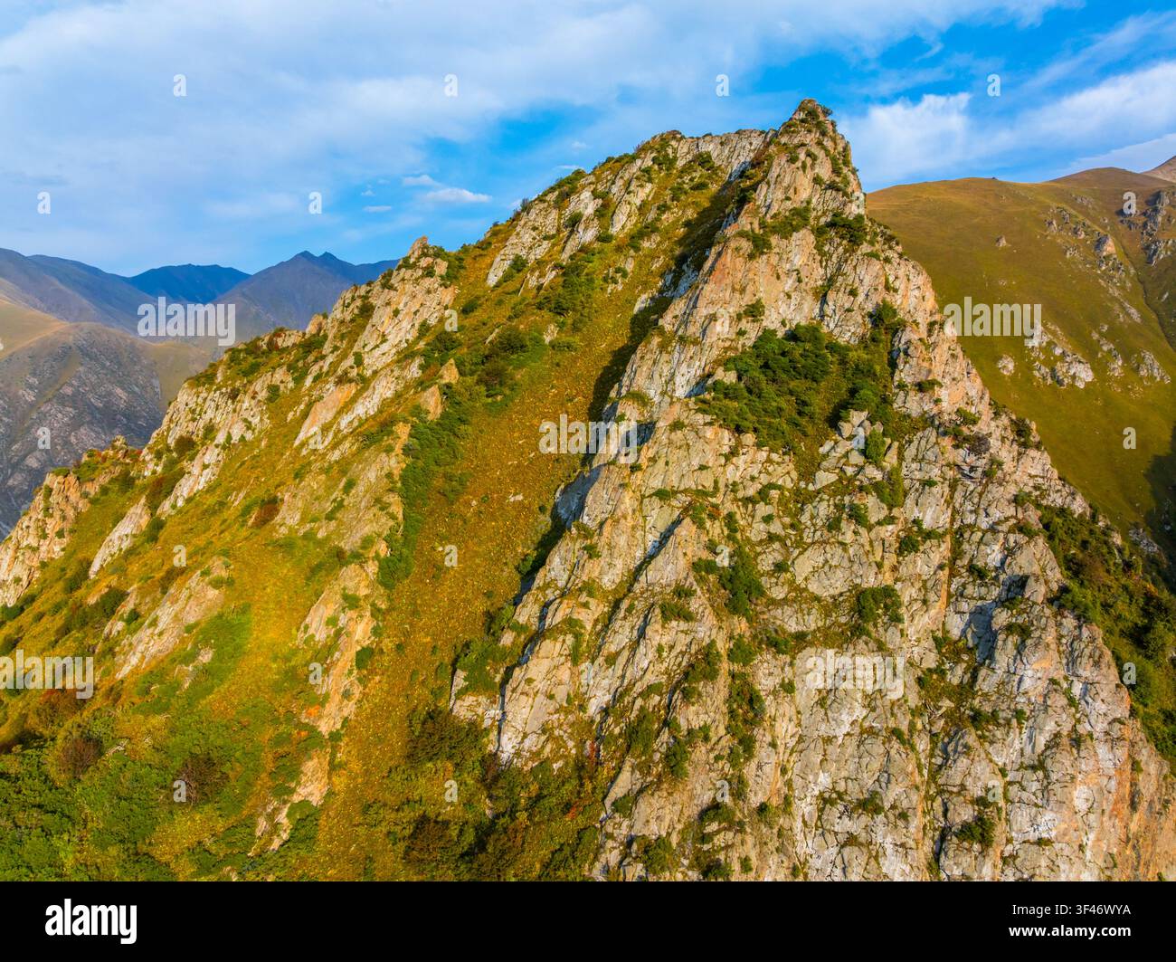 Luftaufnahme zeigt eine raue Berglandschaft in Kirgisistan. Steile felsige Hänge sind mit Flecken trockenen Grases und grüner Büsche geschmückt, die zu Stockfoto