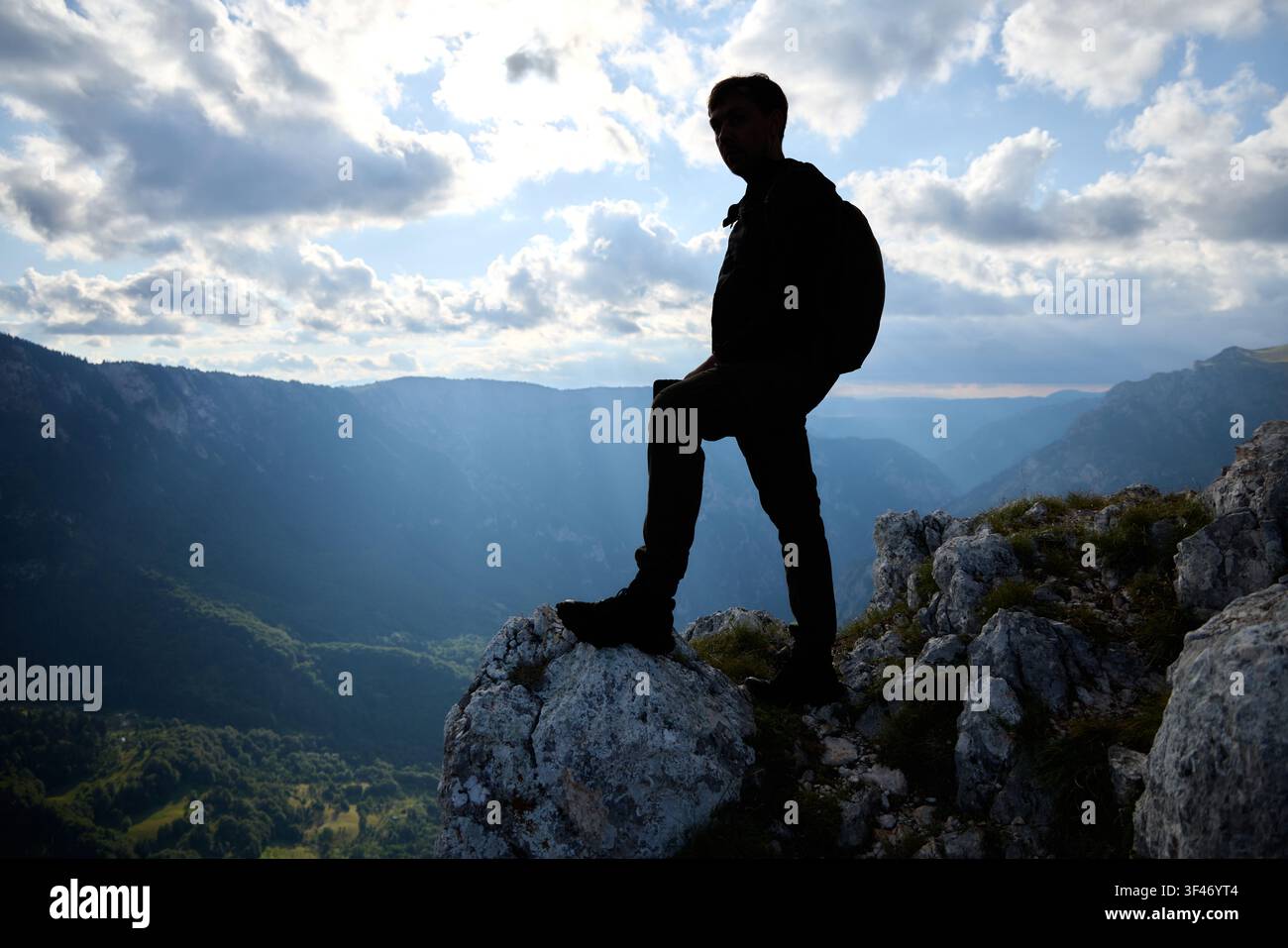 Der Mann steht selbstbewusst am Rand, vor dem Hintergrund des späten Sonnenlichts und der fernen Berge. Das Bild vermittelt Größe und Einsamkeit. Stockfoto