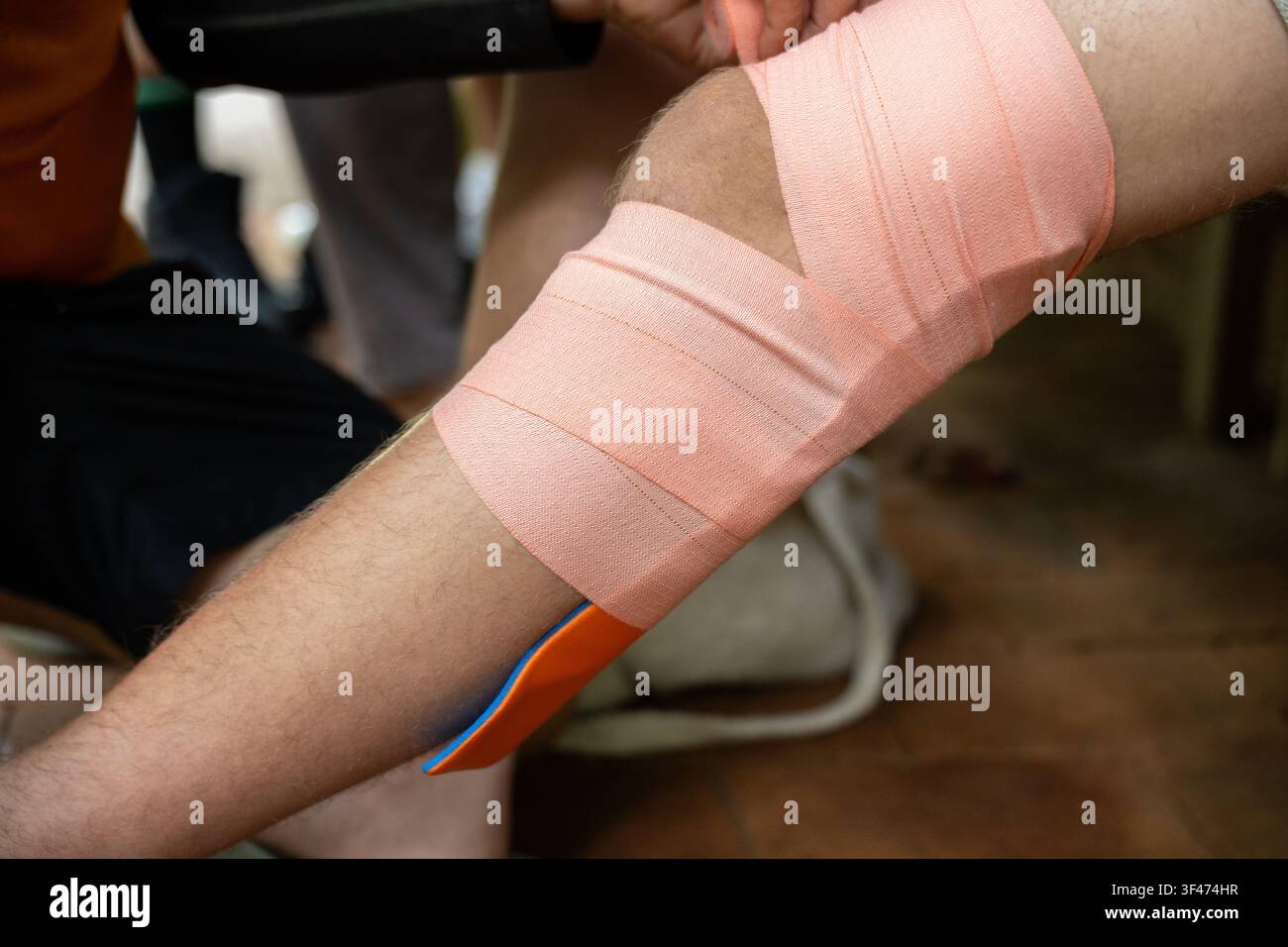 Ein elastisches therapeutisches Pflaster, das um ein gebeugtes Knie in einer Sport-First-Aid-Umgebung gewickelt ist, zeigt Unterstützung bei Sportverletzungen und ruhige Pflege Stockfoto