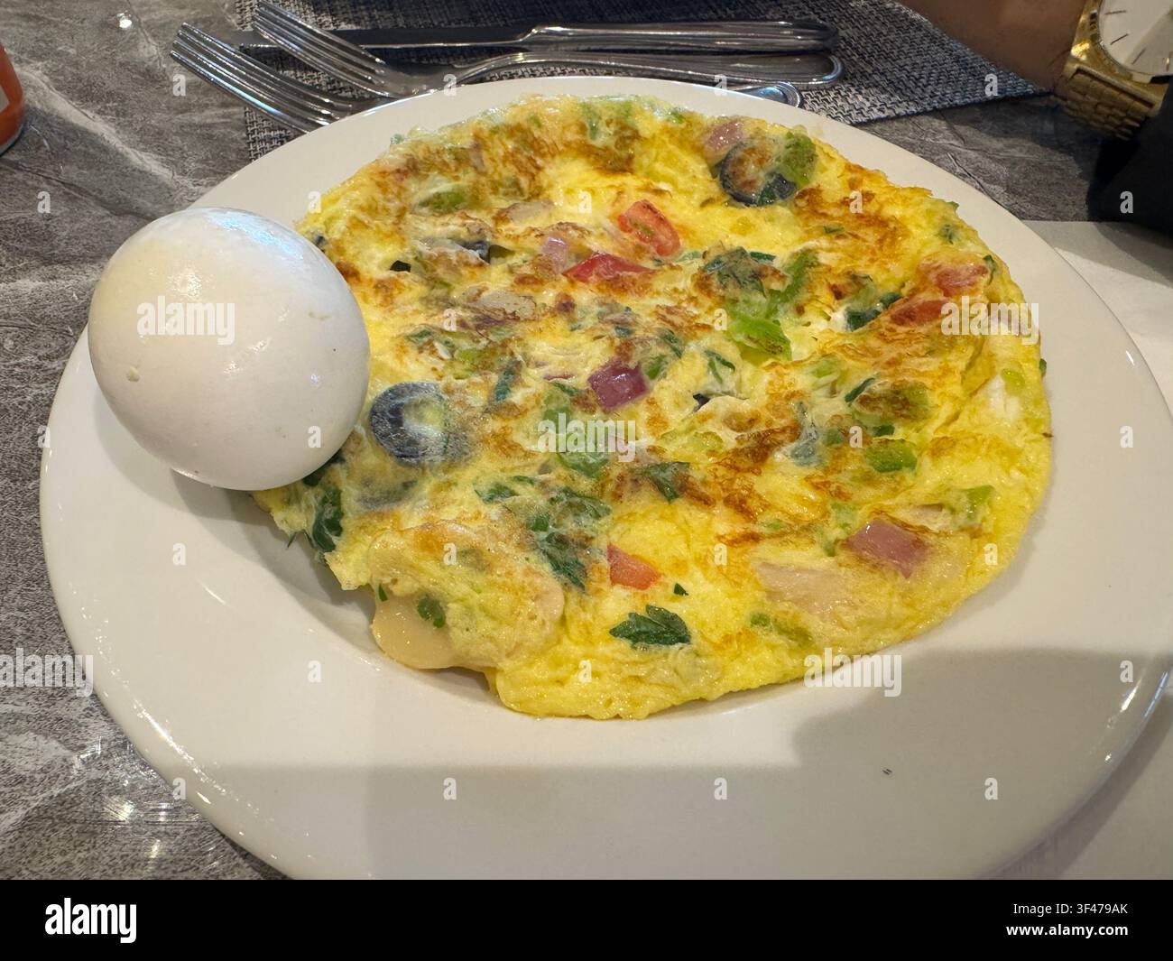 Ein herzhaftes Gemüse-Omelett, serviert mit einem gekochten Ei auf einem weißen Teller, geeignet für ein nahrhaftes Frühstück oder eine gesunde Mahlzeit. Stockfoto
