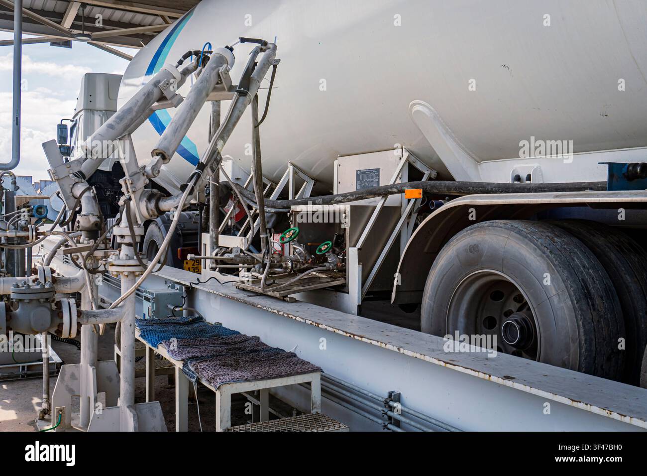 LNG- oder Flüssiggastankwagen, der an eine Tankstelle angeschlossen ist, zeigt komplexe Rohrleitungen, Ventile und Schlauchverbindungen entlang der Seite des Tankwagens an einem Stockfoto