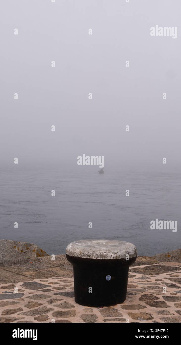 Eiserner Festmacherpfahl an einem steinernen Kai mit Blick auf ein nebelverhangenes Meer, Portugal Stockfoto