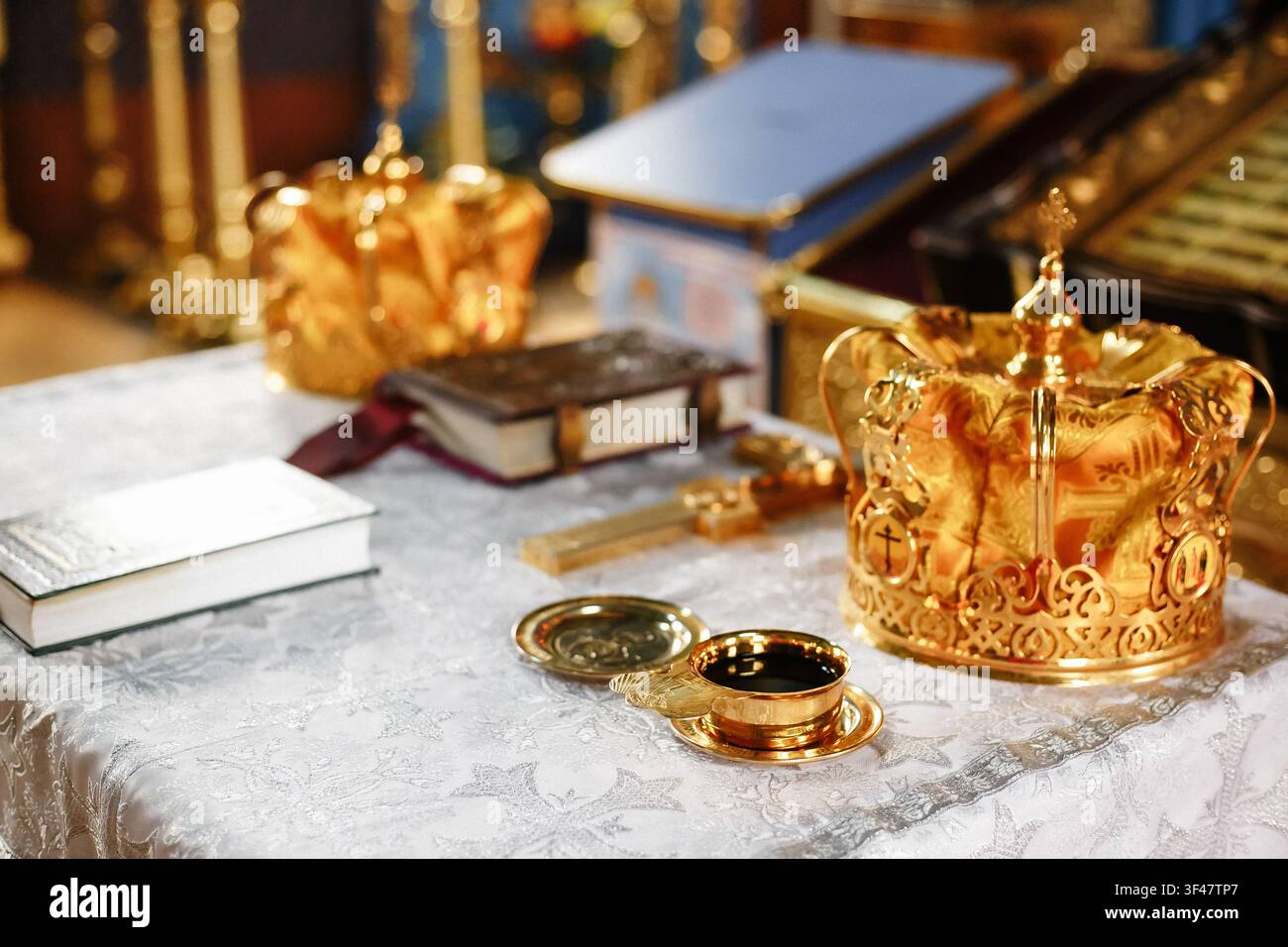 Verschnörkelte goldene Kronen für eine orthodoxe Hochzeitszeremonie und ein heiliges religiöses Buch auf einem Tisch. Traditionelles christliches EheSakrament, Kirchenaltar-Aufbau Stockfoto