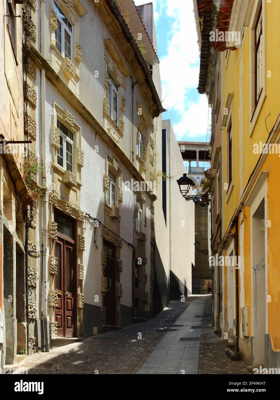 Eine sehr schmale historische Straße in Coimbra, gesäumt von alten mittelalterlichen Häusern, wo sich traditionelle Architektur mit modernen Gebäuden vermischt und freiliegende Elektroleitungen Stockfoto