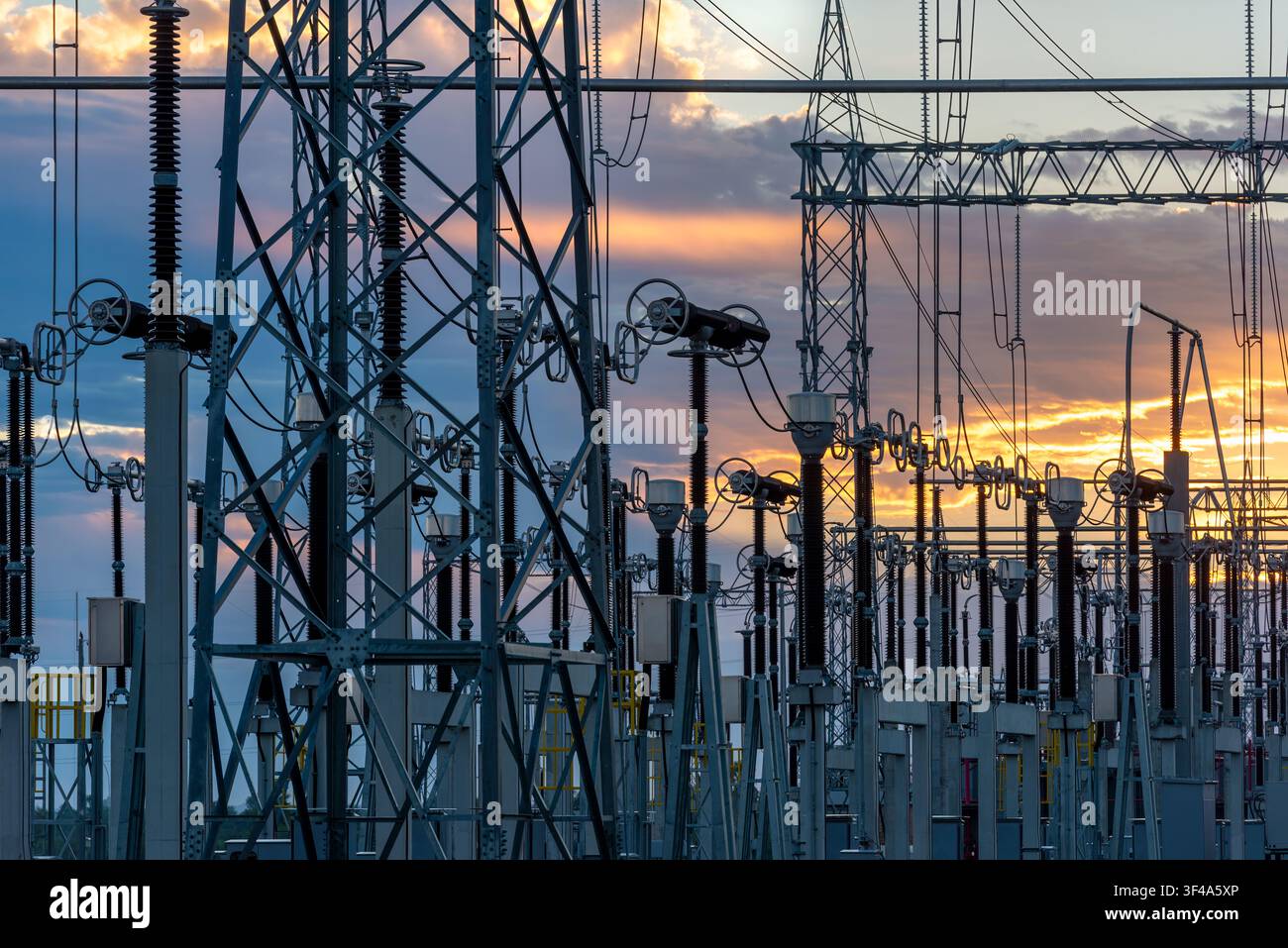 Ein Umspannwerk mit Stahltürmen, Transformatoren und Stromleitungen vor einem goldenen Sonnenuntergangshimmel in Villa Hayes, Paraguay. Stockfoto