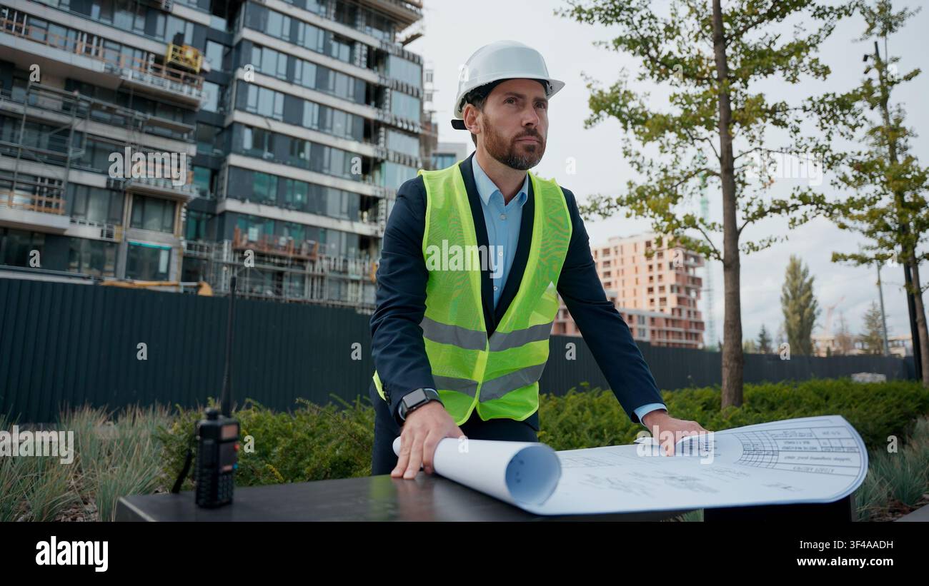 Kaukasischer Mann, Bauingenieur im Helm, betrachtet den Bauplan eines Gebäudeprojekts der städtischen Stadtentwicklung, Geschäftsmann mit Sicherheitshelm Stockfoto