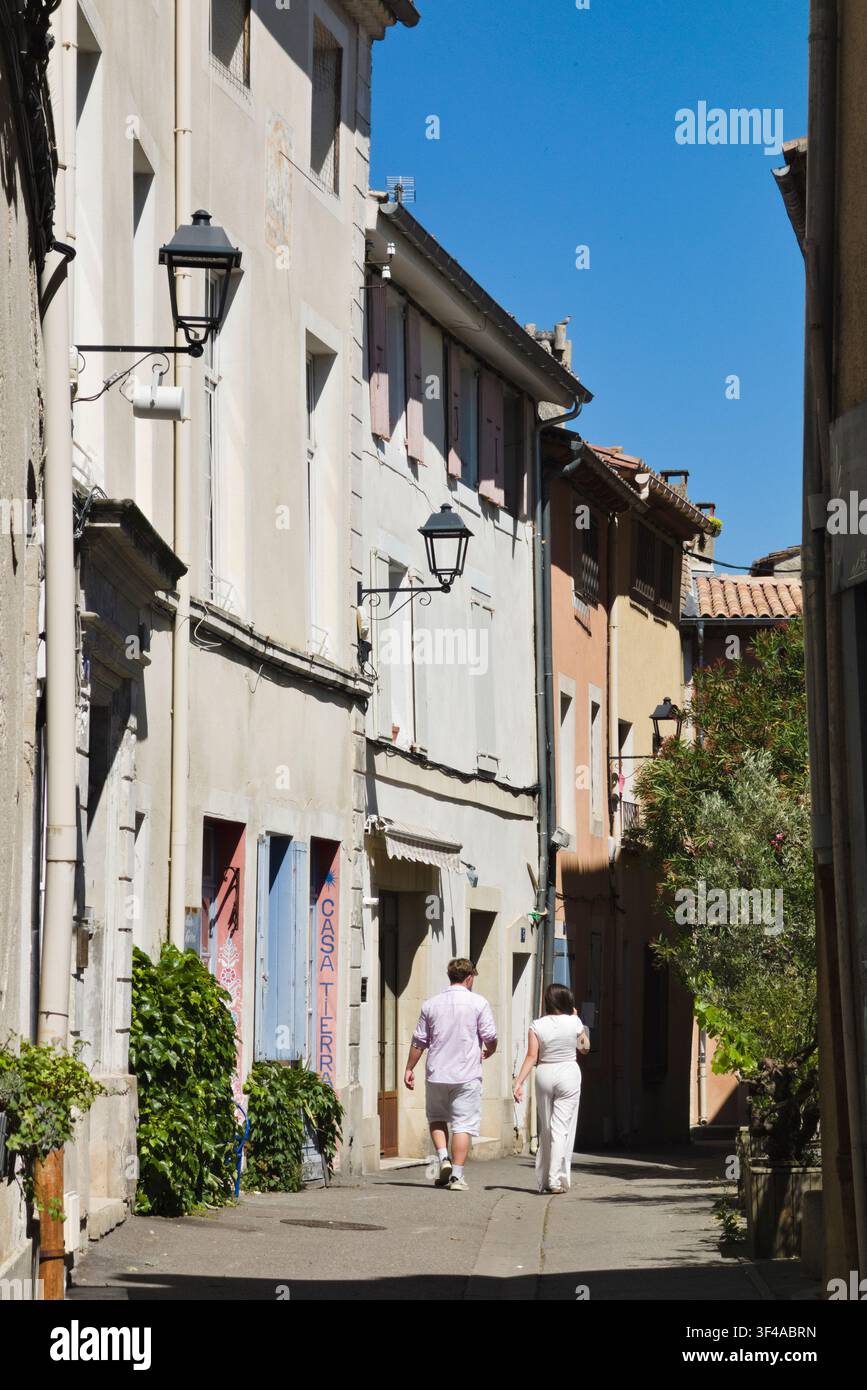Ein Paar geht eine ruhige, schmale Kopfsteinpflastergasse entlang, die mit traditionellen provenzalischen Häusern gesäumt ist, in L'Isle-sur-la-Sorgue, Frankreich. Stockfoto