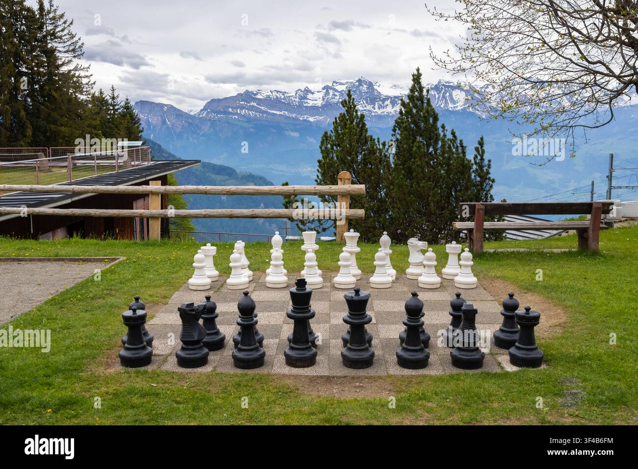 Riesige Schachfiguren, die auf einem Außenschachbrett angeordnet sind, vor einer malerischen Bergkulisse Stockfoto