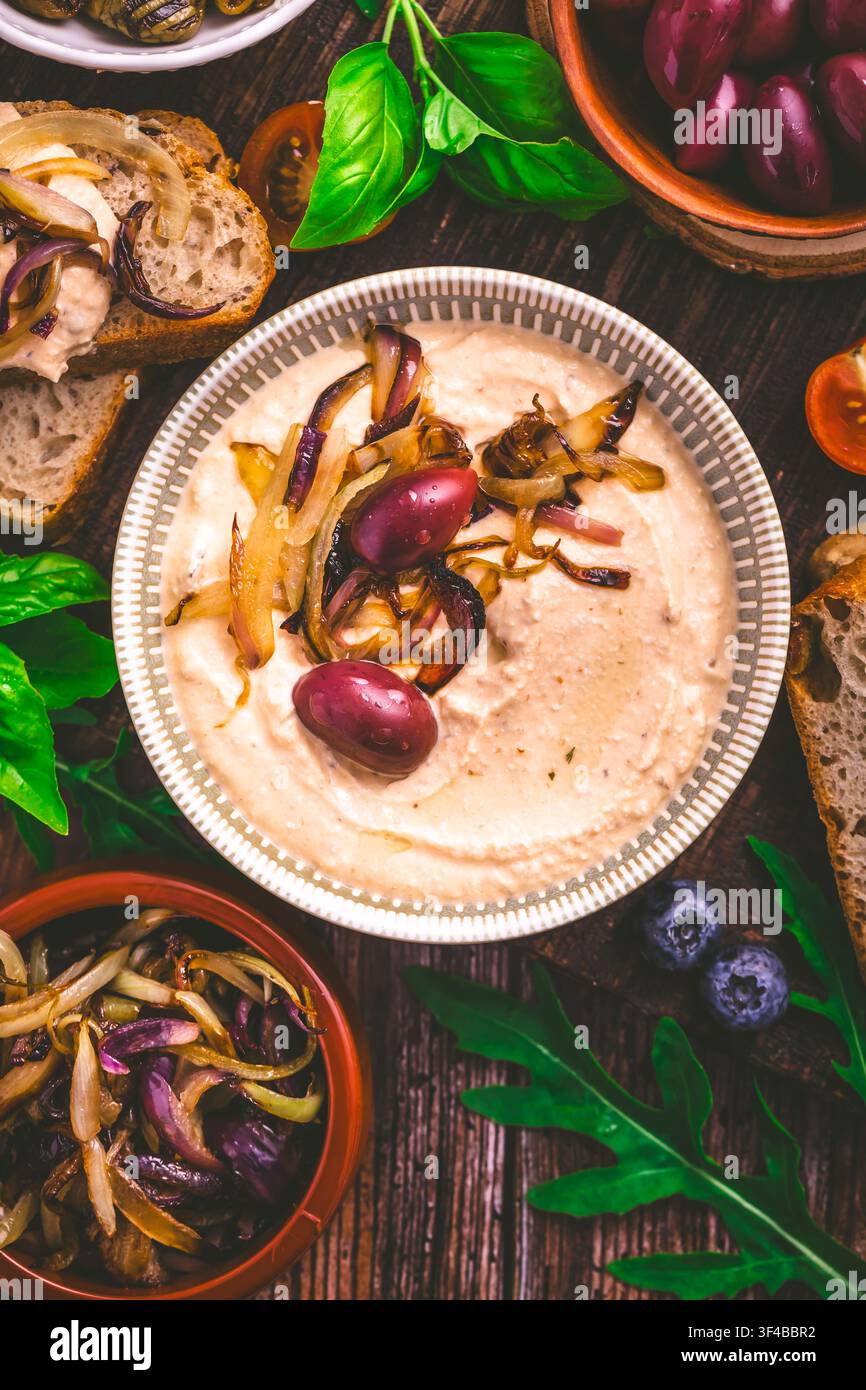 Köstlicher Hummus mit karamellisierten Zwiebeln, Oliven und frischem Brot auf einem Holztisch Stockfoto