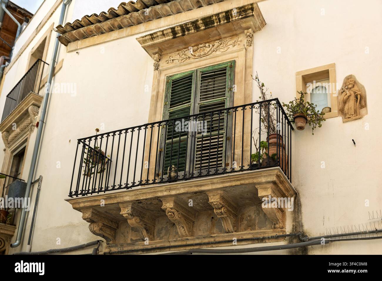 Gebäude mit Balkon, kunstvollen Steindetails, grünen Fensterläden, Topfpflanzen und religiöser Wanddarstellung, Via Francesco Mormina Penna, Scicli, Sizilien, Ita Stockfoto
