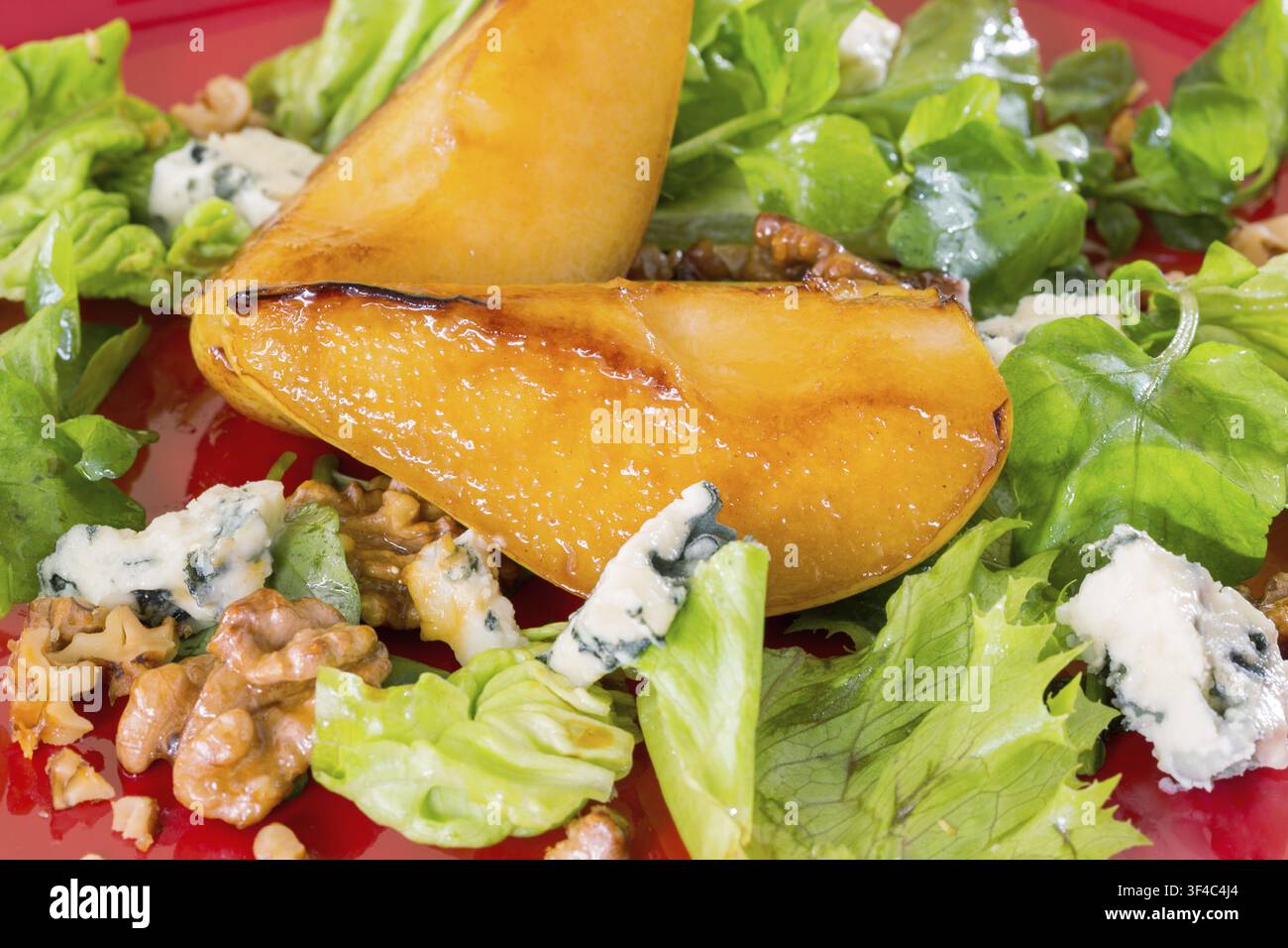 Salat mit karamellisierten Birnen, Walnüssen und Blauschimmelkäse auf rotem Teller Stockfoto