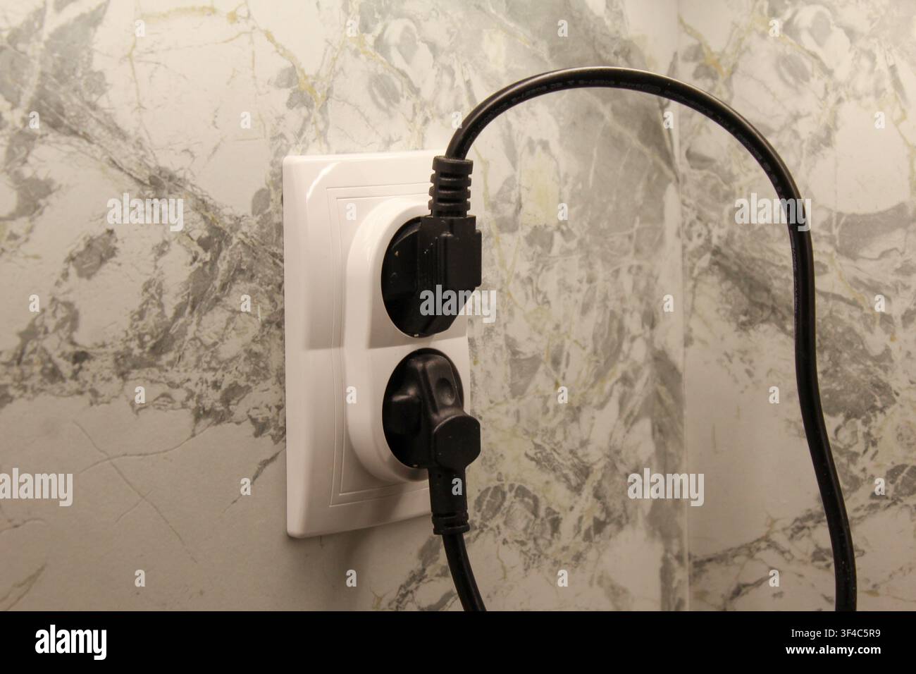 Doppelte europäische Wandsteckdose mit eingesteckten Stromkabeln an einer Marmorwand. Konzept für Hausstrom, Energieversorgung und elektrischen Anschluss. Stockfoto