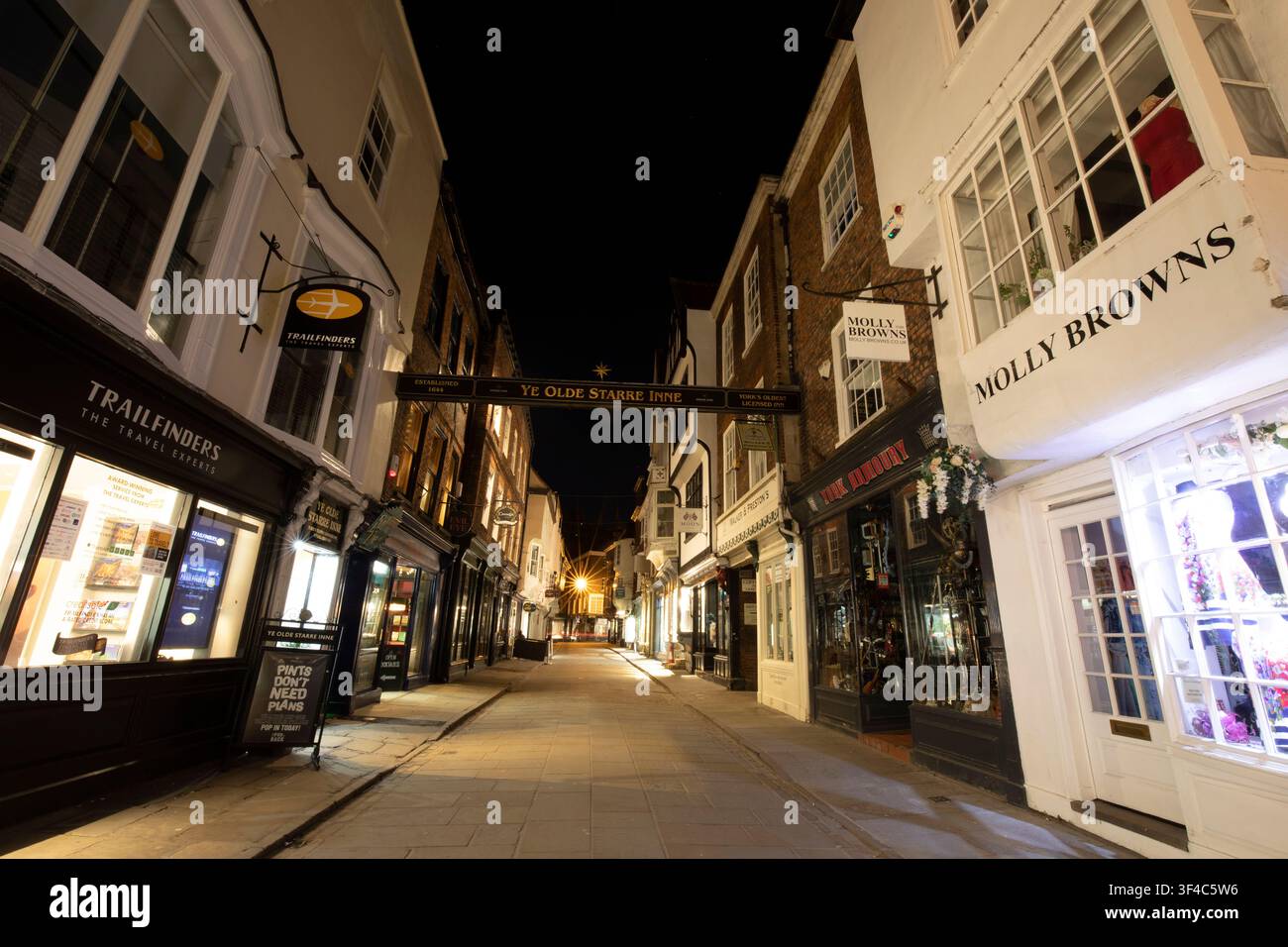 Beleuchtete historische Schaufenster und das ikonische überdachte Galgenzeichen des Ye Olde Starre Inne entlang der Stonegate bei Nacht in der Stadt York, UK. Stockfoto