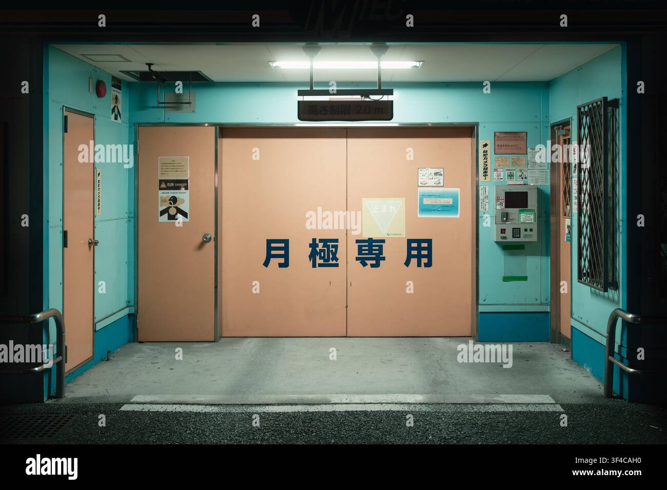 Geschlossenes türkisfarbenes Metallschloss eines automatisierten Tiefgarage-Eingangs mit Kanji-Text unter einer Türlampe bei Nacht, Osaka, Japan. Stockfoto