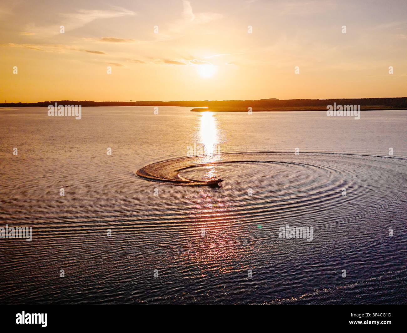 Motorboot erzeugt kreisförmige Spiralwellen auf einem See während des Sonnenuntergangs Stockfoto