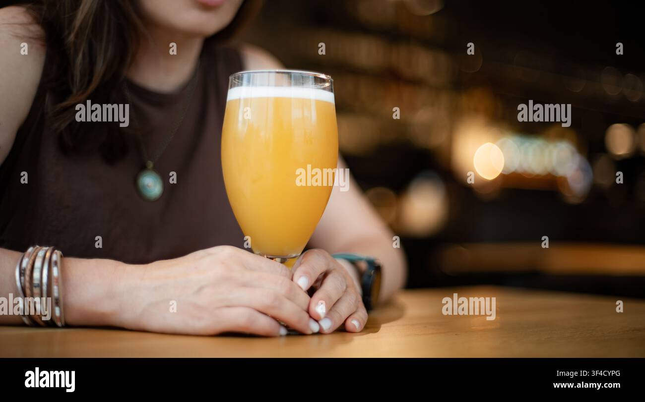 Frau genießt Weizenbier an einem Tisch in einem überfüllten Pub Stockfoto