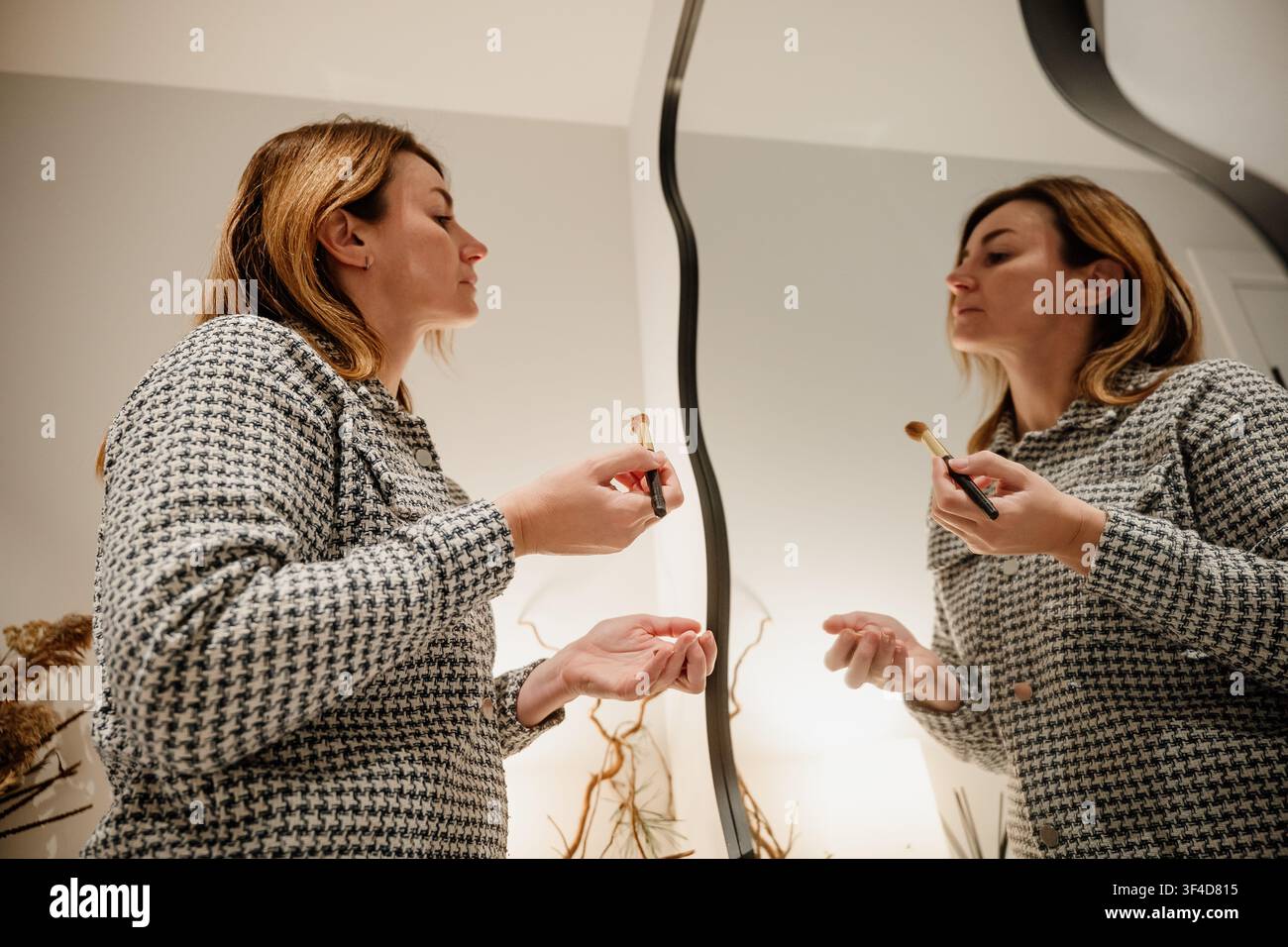 Frau, die abends zu Hause vor einem Spiegel Make-up aufträgt Stockfoto
