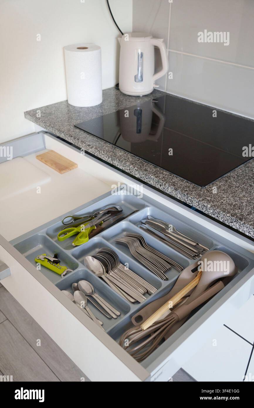 Offener Küchenschrank, der mit Besteck, silbernen Utensilien und Kochwerkzeugen unter einer modernen Arbeitsplatte organisiert ist Stockfoto