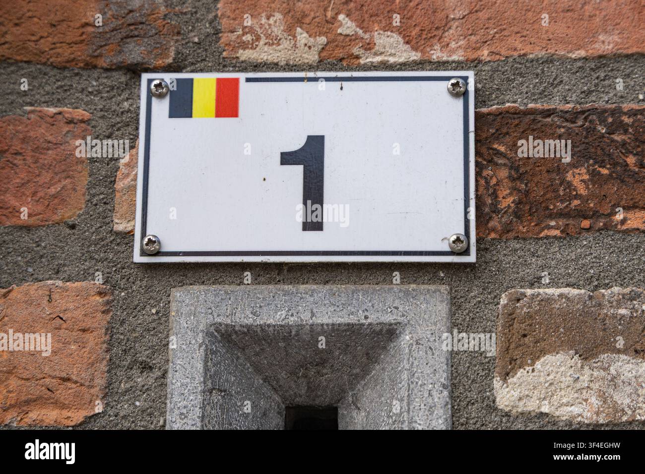 Ansicht eines Hausnummernschilds mit der Nummer eins und einer kleinen belgischen Flagge, die an einer rustikalen Ziegelwand in Baarle-Hertog, Flandern, Belgien, angebracht ist. Stockfoto