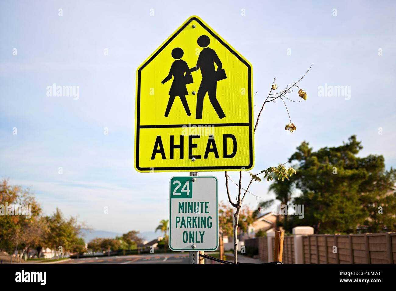 Gelbes Fußgängerüberweg-Schild warnt Fahrer vor einer Schulzone voraus entlang einer ruhigen Vorstadtstraße bei klarem Tageslicht. Stockfoto