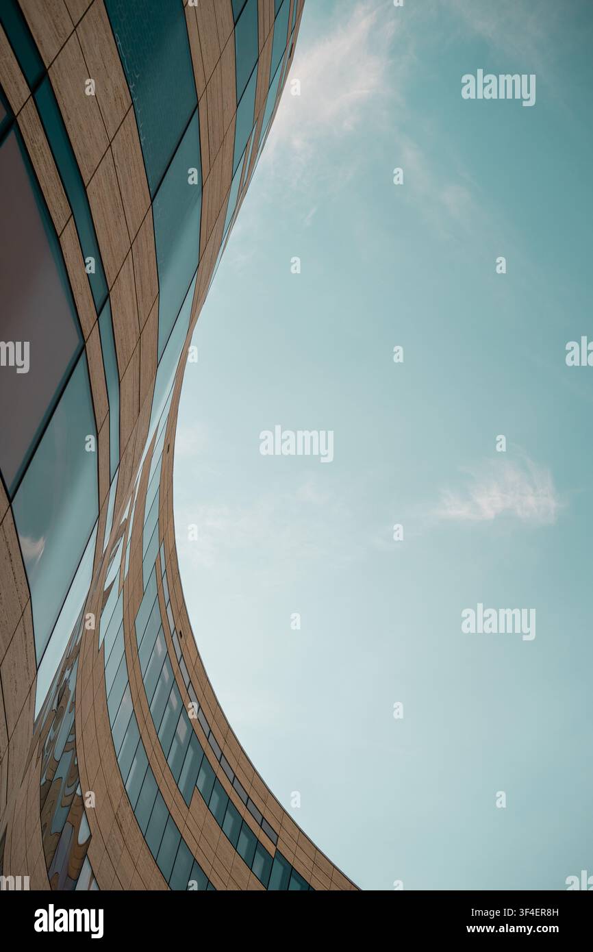 Dramatische gebogene moderne Gebäudefassade mit großem freiem Himmel als Kopierraum, vertikale Ansicht Stockfoto