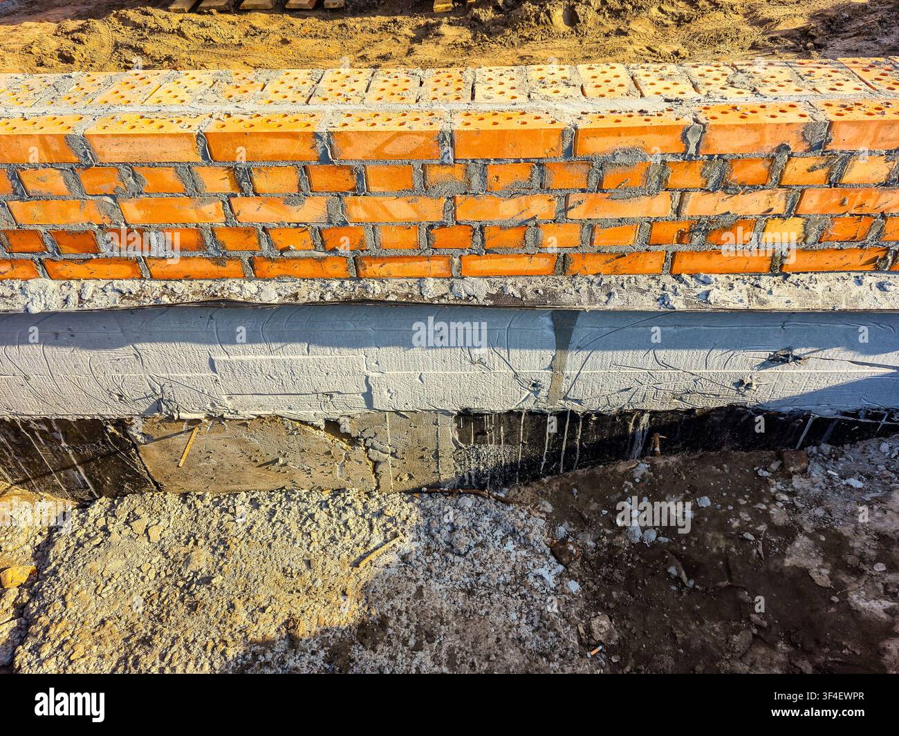 Nahaufnahme einer Gebäudefundierung im Bau, mit orangefarbenem Mauerwerk und Betonelementen Stockfoto