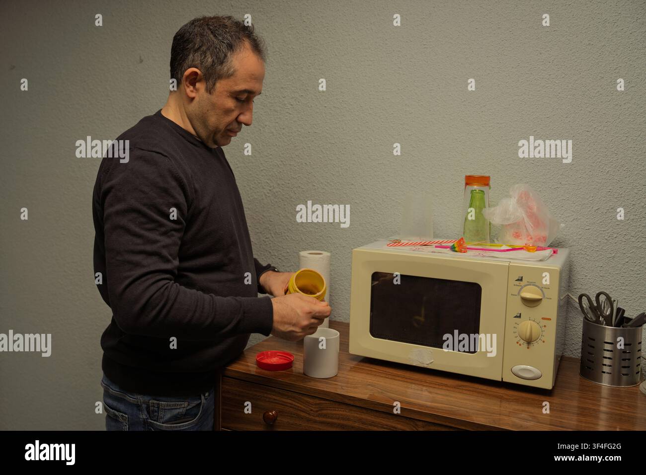 Mann bereitet Instantkaffee in einer Tasse neben einer Mikrowelle auf einer Holzkommode zu Stockfoto