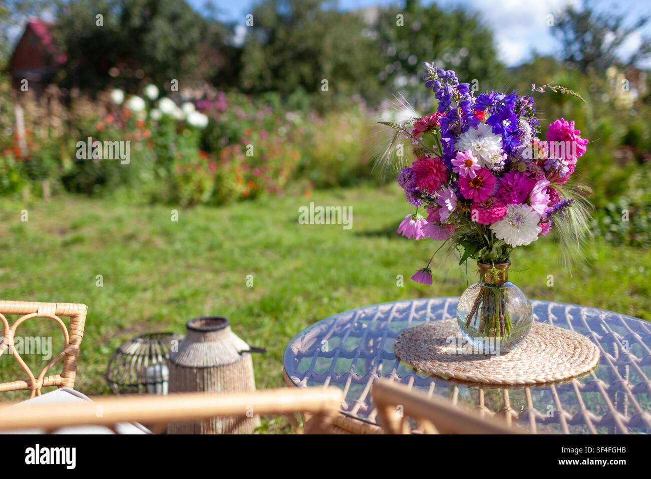 Nahaufnahme eines Blumenarrangements, das auf einem Glastisch im Sommergarten steht. Lounge-Bereich mit Möbeln und Strauß frischer Blumen in einer Vase Stockfoto