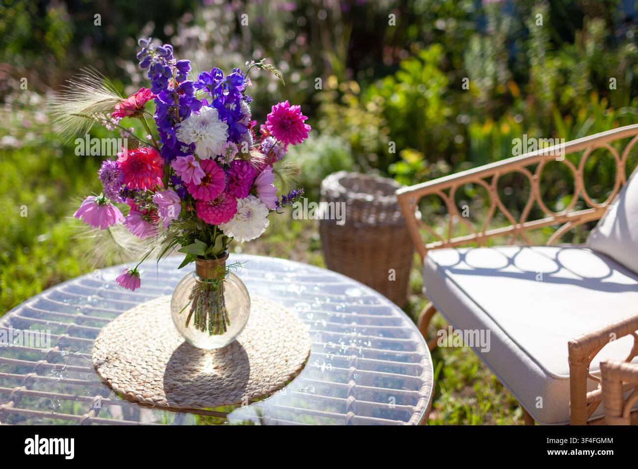 Nahaufnahme eines Blumenarrangements, das auf einem Glastisch im Sommergarten steht. Lounge-Bereich mit Möbeln und Strauß frischer Blumen in einer Vase Stockfoto