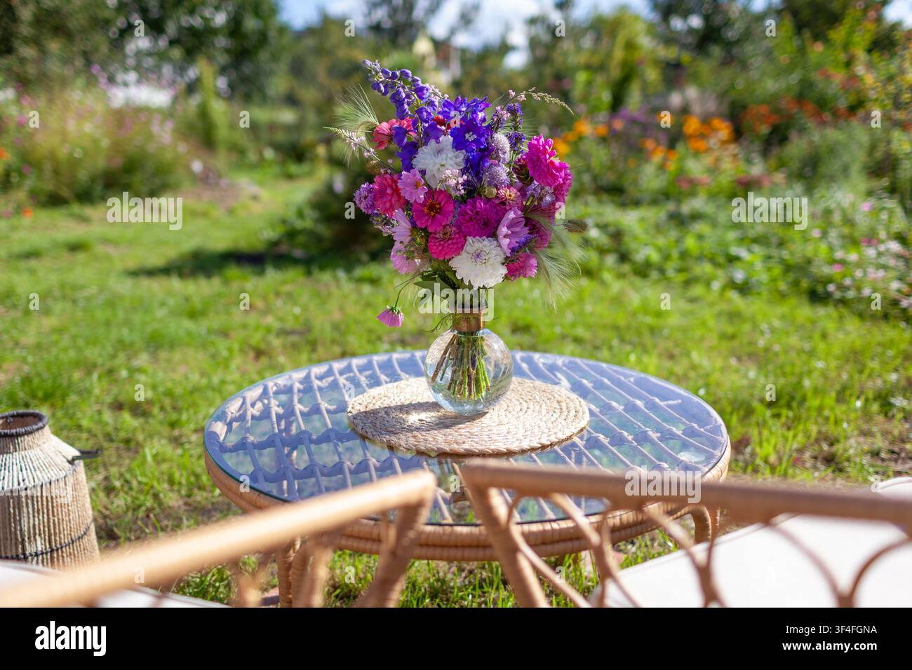Nahaufnahme eines Blumenarrangements, das auf einem Glastisch im Sommergarten steht. Lounge-Bereich mit Möbeln und Strauß frischer Blumen in einer Vase Stockfoto