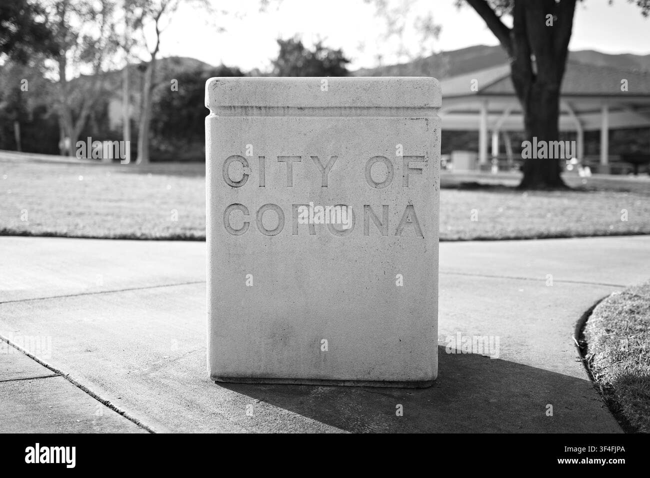 Ein Beton-Stadtmarker mit der Gravur „City of Corona“ steht in einem öffentlichen Park und unterstreicht die lokale Identität und den öffentlichen Raum in Corona, Kalifornien. Stockfoto