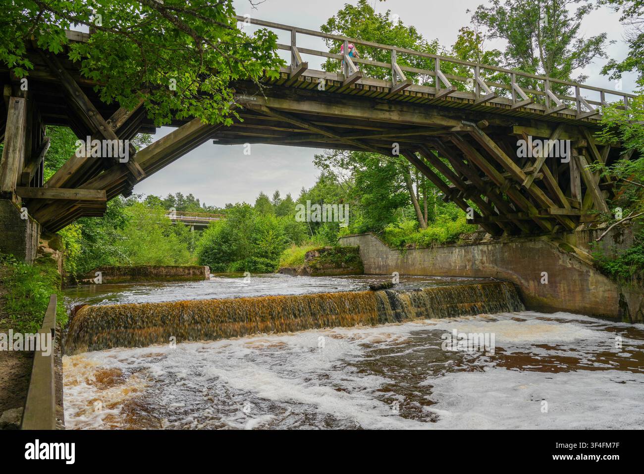Historische Holzbrücke über den Riva-Fluss mit kleinem Wasserfall in der malerischen Landschaft des lettischen Landes Stockfoto