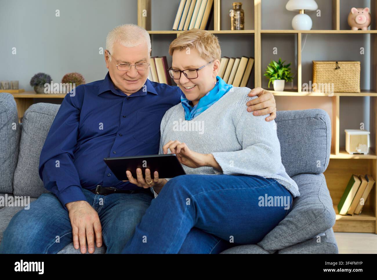 Lächelndes Seniorenpaar, das gemeinsam zu Hause auf einer bequemen Couch ein Digitales Tablet nutzt Stockfoto