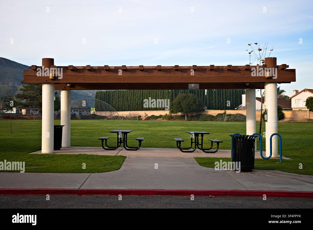 Offener Parkpavillon mit Picknicktischen und schattigen Sitzgelegenheiten, der auf einem Grashalm mit Bergen und Bäumen im Hintergrund steht. Stockfoto