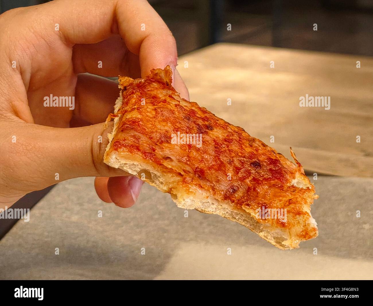 Frauenzhand, die eine kleine Scheibe knusprige Käsepizza hält - Smartphone-aufgenommenes Stockfoto