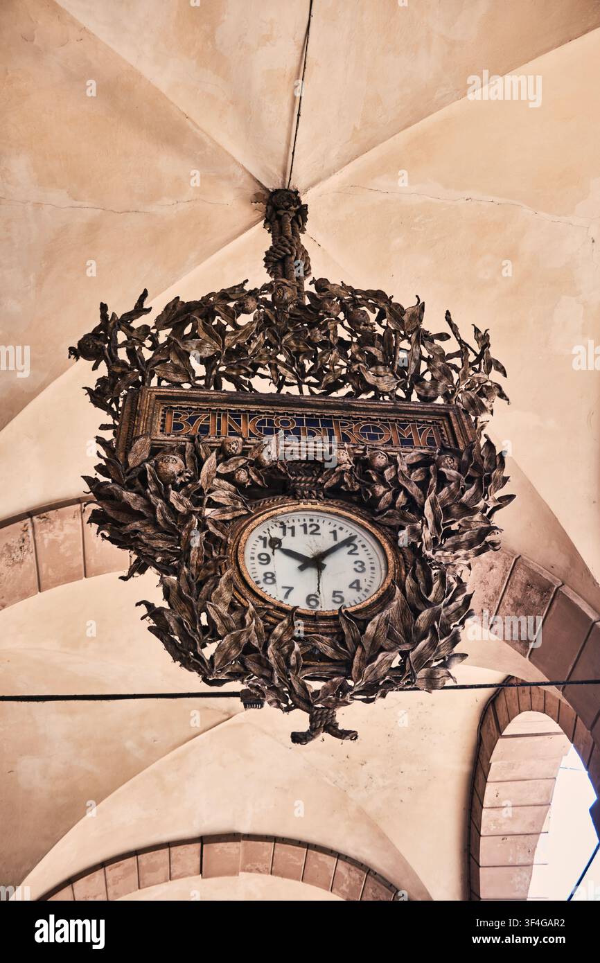 Bologna, Italien - Mai 2026: Aufwendige schmiedeeiserne Zieruhr, die unter einer gewölbten historischen Portikusdecke hängt Stockfoto