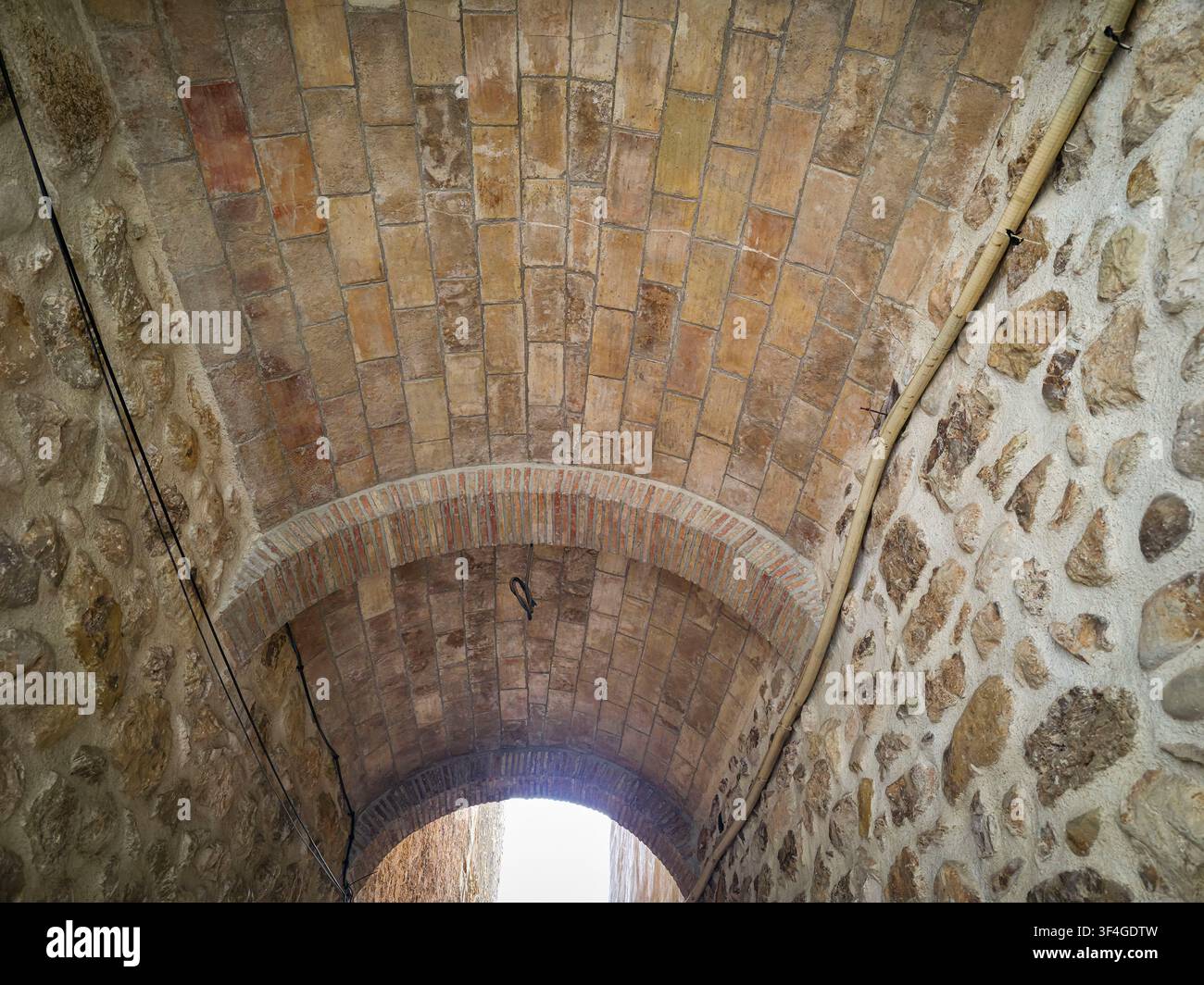 Ein Ziegelbogen, von unten betrachtet. Steinmauern säumen den Tunnel. Licht dringt durch die Öffnung am Ende des Durchgangs ein. Die Architektur zeigt sein Stockfoto