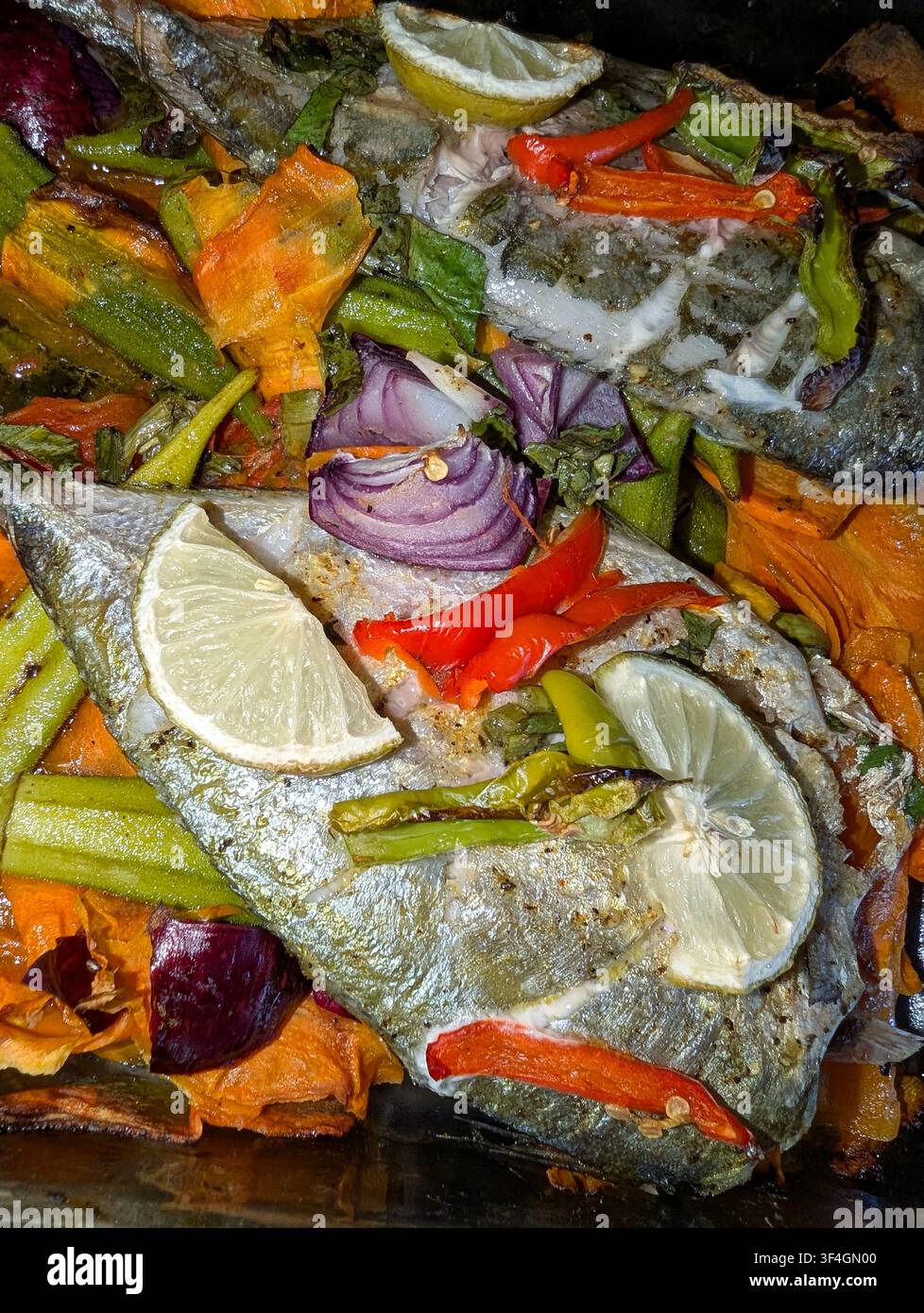 Ein frisch gebackenes Fischgericht, gekocht mit Gemüse wie Karotten, Paprika, roten Zwiebeln, Okras, Tomaten und garniert mit Limettenscheiben. Stockfoto