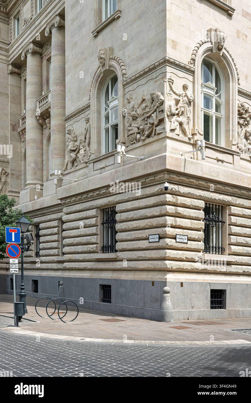 Die rustizierte Steinecke der Ungarischen Nationalbank trifft auf eine ruhige Kopfsteinpflasterstraße mit gewölbten Fenstern, geschnitzten Reliefs und einem Straßenschild Stockfoto