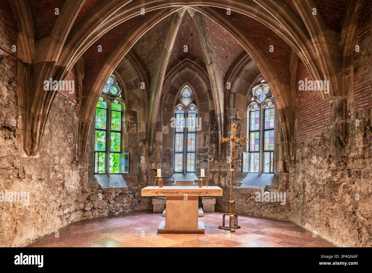 Das Sonnenlicht fällt durch schmale Buntglasfenster auf die Rippengewölbe einer mittelalterlichen gotischen Kapelle, wo ein Steinaltar mit Kerzenständern und einem Stockfoto