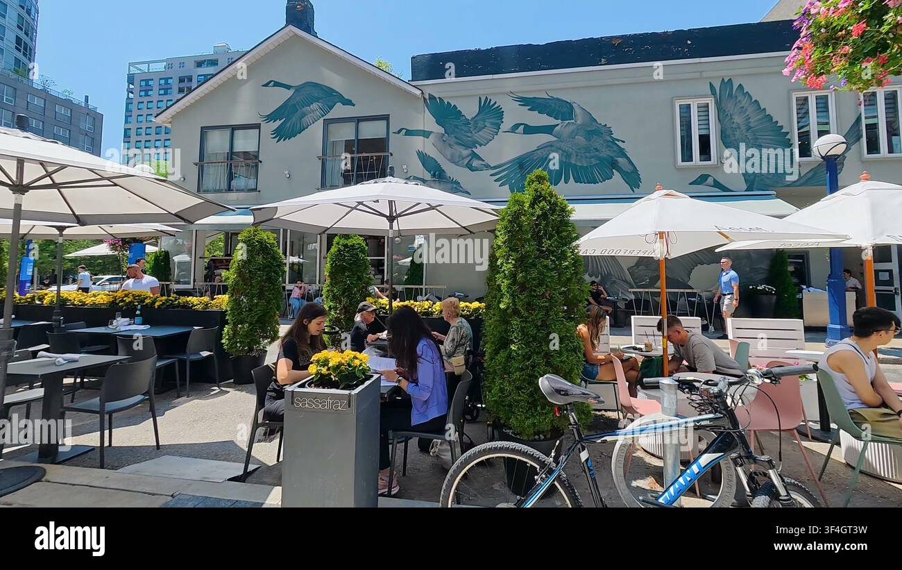 TORONTO, KANADA - 15. JUNI 2024: Gäste genießen Essen und Getränke unter Sonnenschirmen auf der Terrasse eines Restaurants im Stadtteil Yorkville von Toronto. Stockfoto