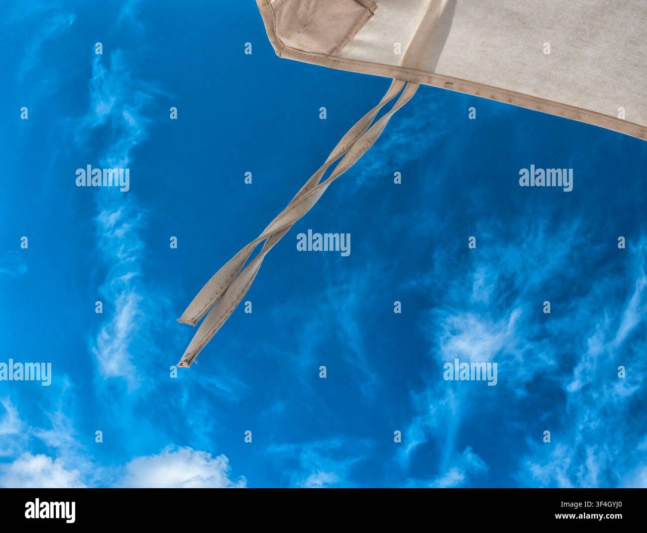 Ein beiger Strandschirm, der sich gegen einen hellblauen Himmel abhebt. Stockfoto