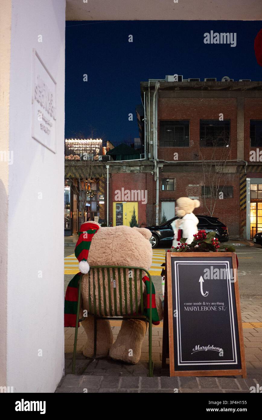 Ein großer Teddybär mit einem Weihnachtsschal sitzt auf einem Stuhl auf einer Straße in Seongsu-dong, Seoul. Stockfoto