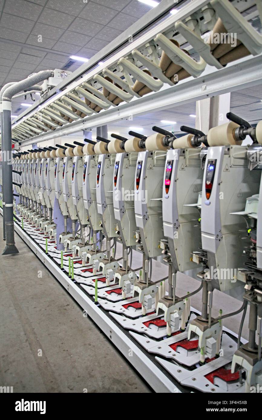 Das Bild zeigt das Innere einer modernen Textilfabrik mit Reihen von ordentlich angeordneten und hocheffizienten automatischen Spulmaschinen. E Stockfoto