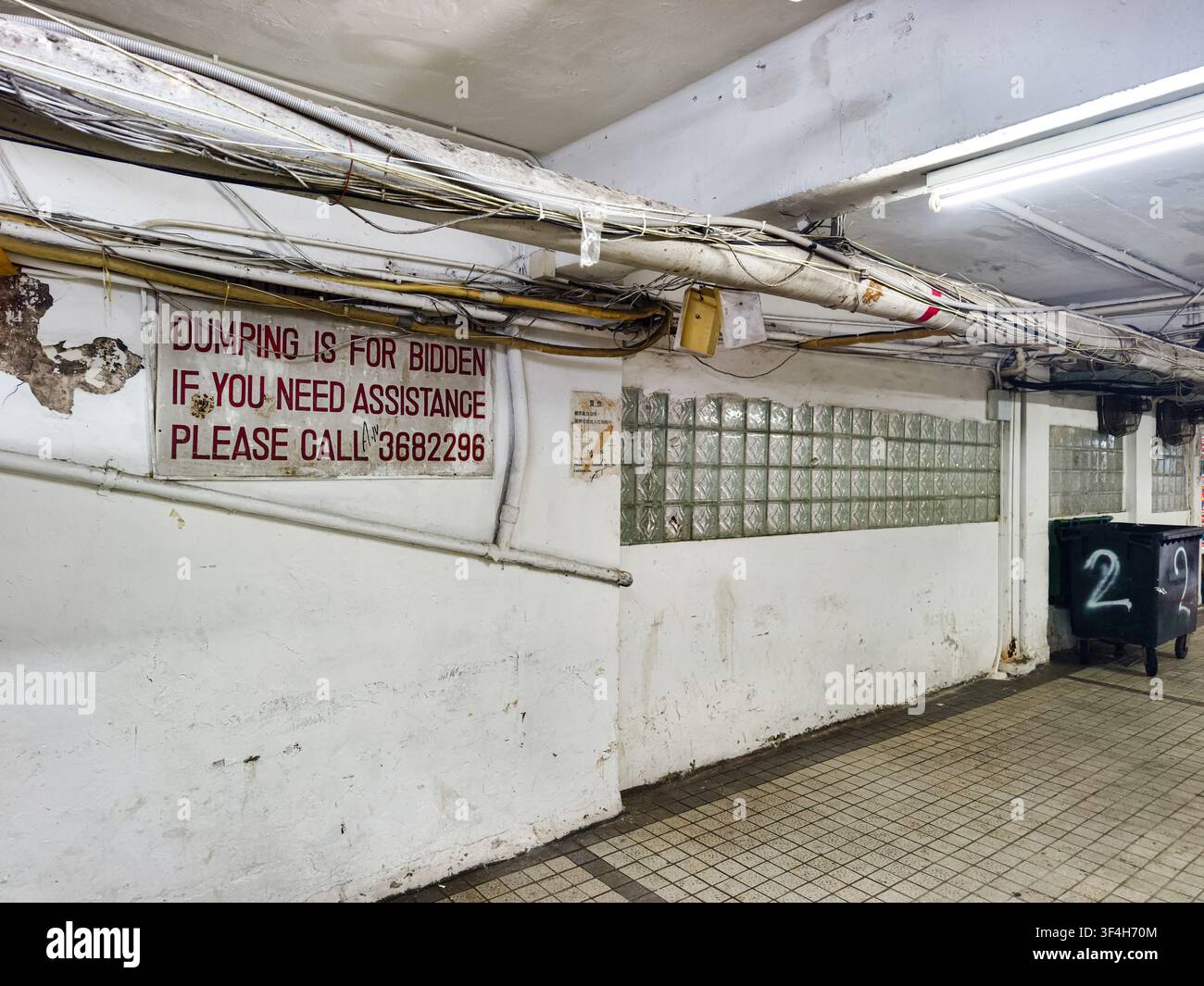 Bereich mit niedriger Decke, dicke Strukturträger und industrieller Neonbeleuchtung, Innengang, Mirador-Villa, Hongkong, Schild „Abfall entsorgen verboten" Stockfoto