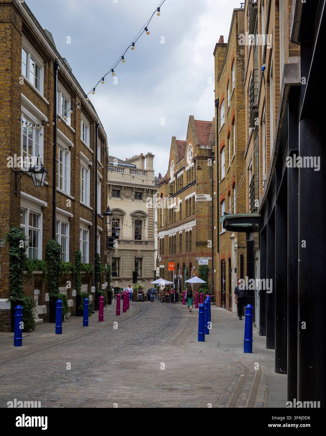 Schmale Kopfsteinpflaster-Passage, gesäumt von historischen Ziegel Fassaden mit großen Fenstern und Efeu an den Wänden. Blaue Poller markieren den Fußgängerweg Stockfoto
