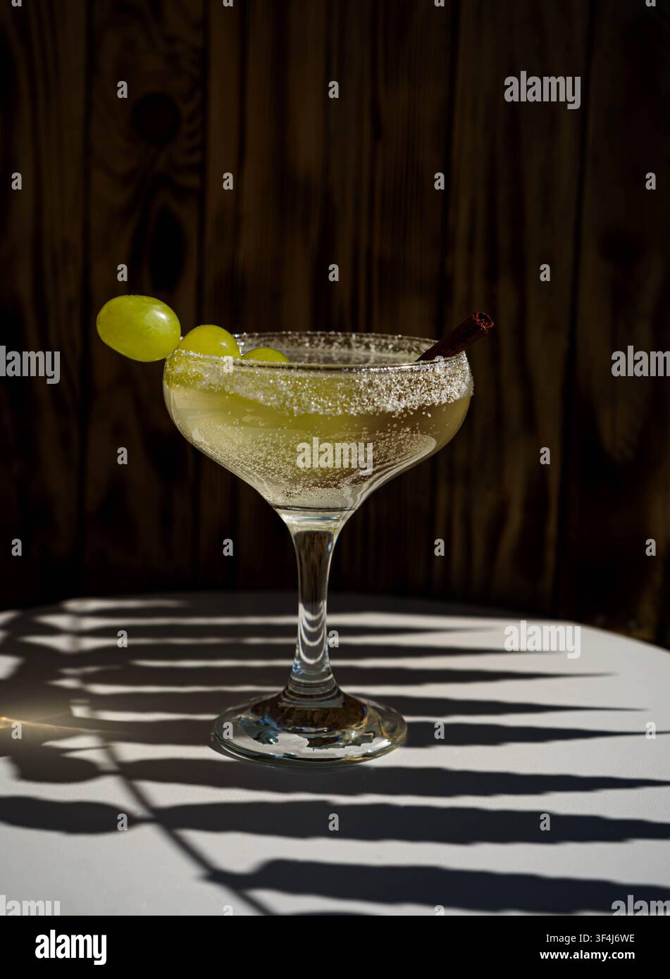 Klassischer Margarita-Cocktail mit gesalzenem Rand und frischen grünen Trauben, serviert in einem Coupé-Glas vor einem rustikalen Holz-Hintergrund. Stockfoto