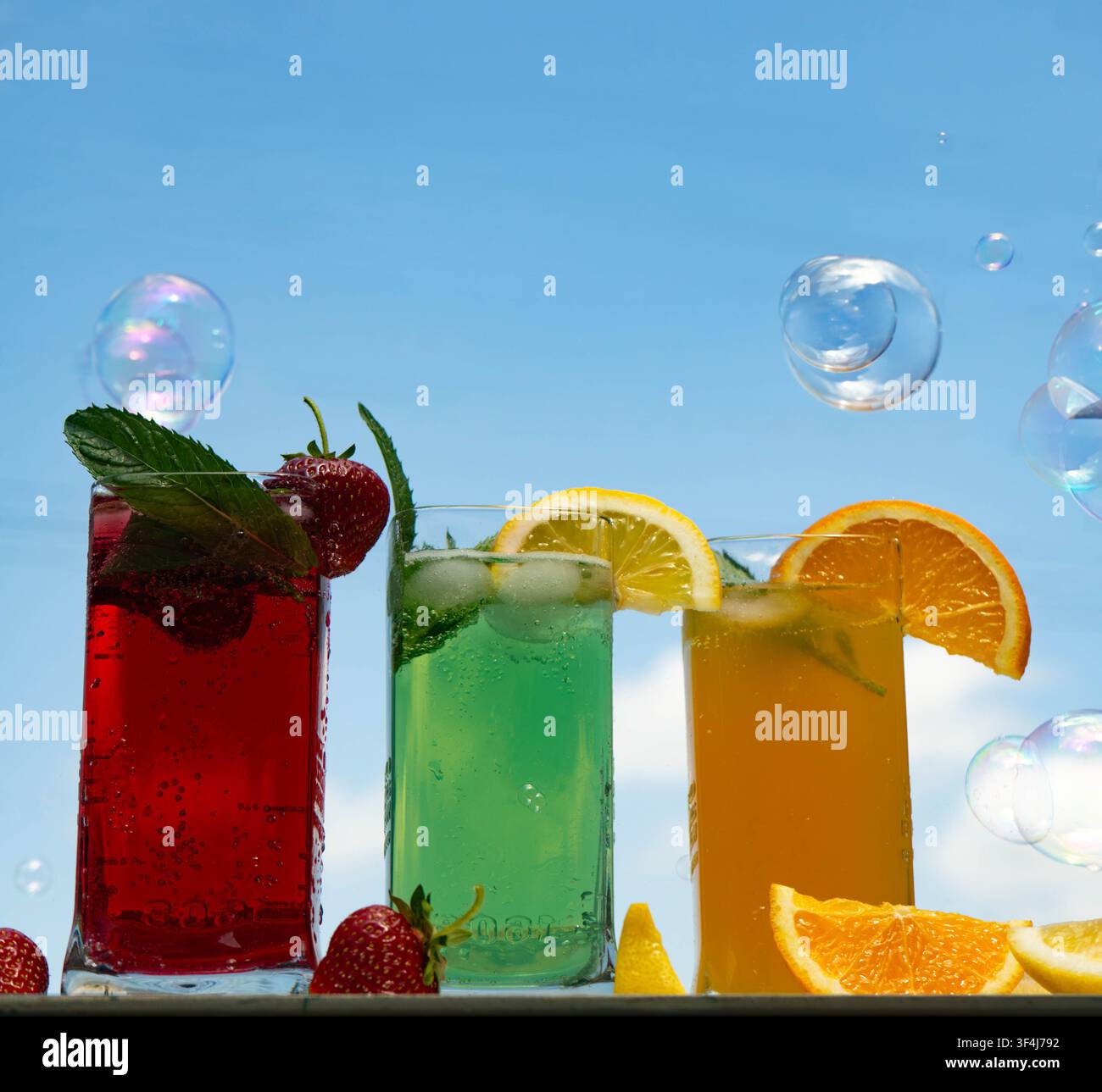 Farbenfrohe erfrischende Sommercocktails mit Zitrusfrüchten, Beeren und Minze, serviert in hohen Gläsern vor einem strahlend blauen Himmel. Tropisches Partygetränk conce Stockfoto