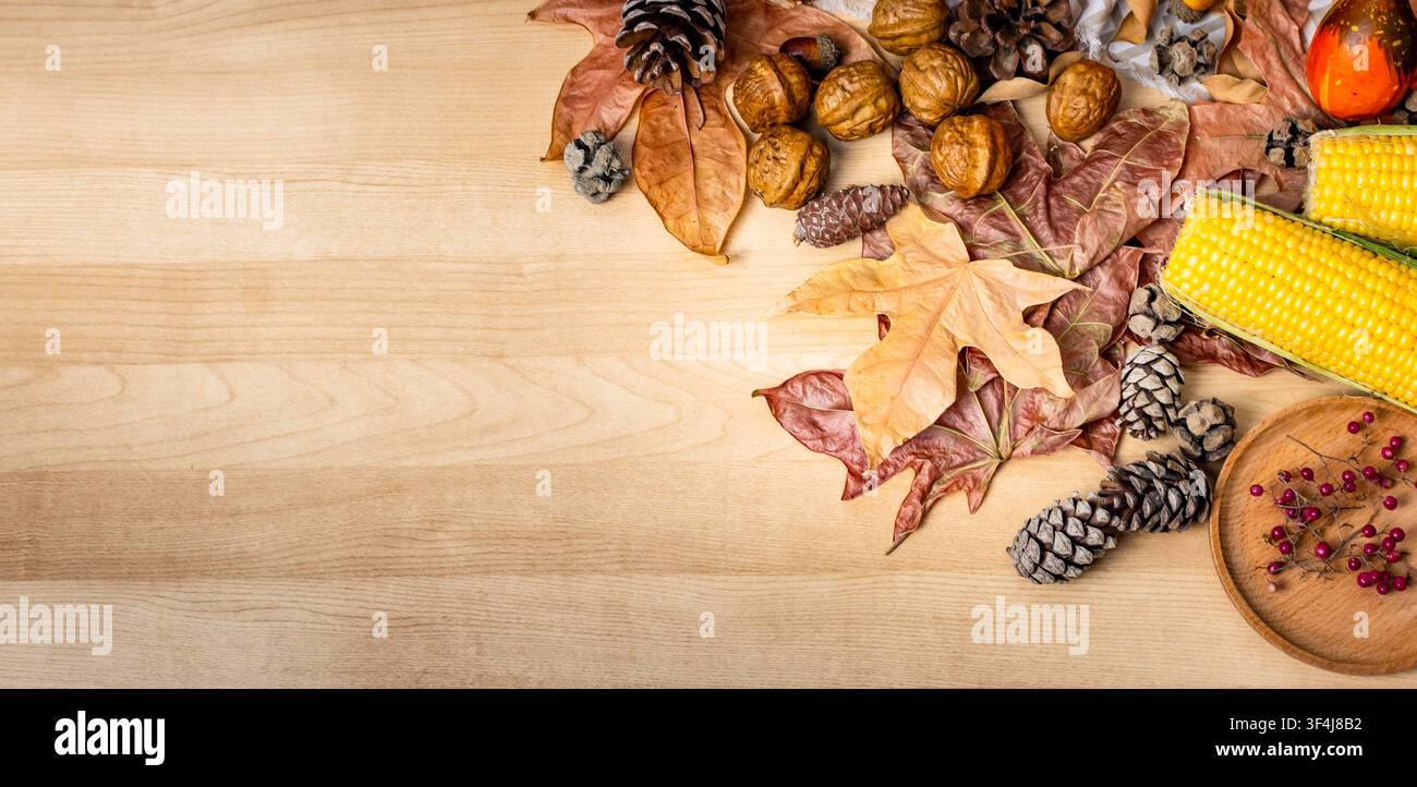 Herbstlicher Hintergrund mit getrockneten Blättern, Maiskolben, Walnüssen und Tannenzapfen auf einer Holzoberfläche Stockfoto
